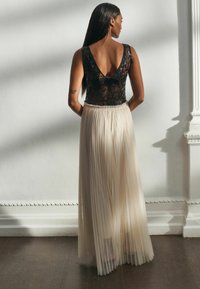 Schwarzer Spitzenbody mit V-Ausschnitt, kombiniert mit einem plissierten, bodenlangen Creme-Rock mit elastischem Bund. Insgesamt glatte Textur.