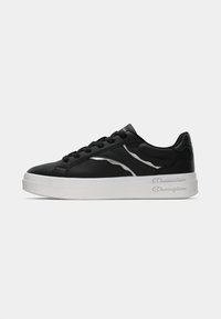 Zapatilla de cuero negro con suela blanca, que presenta delgados acentos plateados y un diseño de cordones. Textura suave con detalles de marca en el talón.