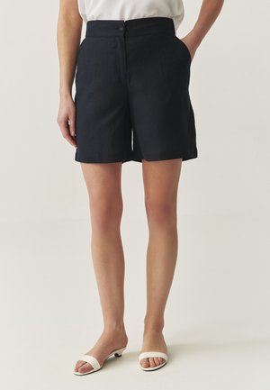 Marineblauwe linnen shorts met een knoopsluiting, zijzakken en een recht gesneden ontwerp, gecombineerd met witte haksandalen.