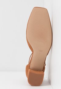 Chaussure en daim marron clair avec un bout effilé, un petit talon carré et une semelle en caoutchouc texturée. Marquée "FABRIQUÉ EN ESPAGNE" sous la semelle.