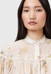 Floral-printed blouse in lightweight cream fabric, featuring a collared neckline, lace trim, button closure, and gathered detailing.