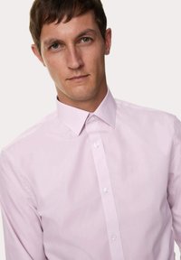 Lichtroze overhemd met knopen, gemaakt van gladde stof, met een klassieke kraag en een voorste pat met knopen. Geen patronen of accenten.