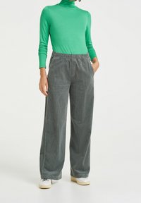 Grön långärmad polotröja i kombination med vida grå kordbyxor med elastisk midja och sidofickor. Vita sneakers synliga.