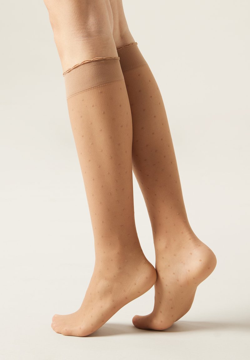 Gennemsigtige nude knæstrømper med små prikker, elastisk kant og glat tekstur. Velegnet til forskellige outfits.