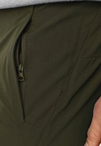 Olivovo zelené látkové cargo nohavice s bočnou zipsovou vreckom, s hladkou textúrou a ostrými ševmi.