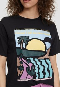 Black t-shirt featuring a colorful graphic design of a sunset, palm trees, and waves with text “Greetings from the sunny side.”