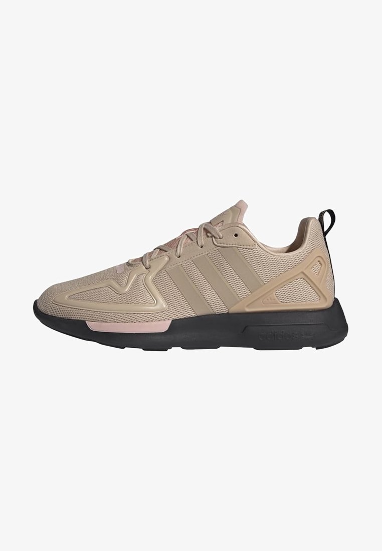 Beige athletic shoes with mesh upper, pink accents, rubber sole, and three stripes design. Features a textured panel and pull tab.