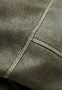 Tmavě šedá kožená látka s hladkým povrchem, vybavená neat švy a záhybem, který ukazuje jemný lesk.