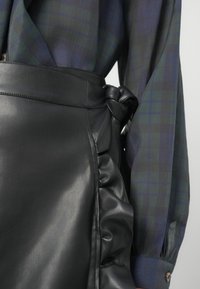 Melna ādas svārku ar ripojošu malu, ar mezgla jostu detaļu. Saskaņota ar zilu un zaļu skotu rakstu blūzi, ar garām piedurknēm.