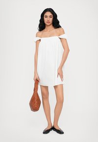 Rochie albă cu umerii descoperiți, cu guler gathered, asortată cu o geantă texturată de culoare maro țesută și cu balerini negri. Design simplu și ușor.