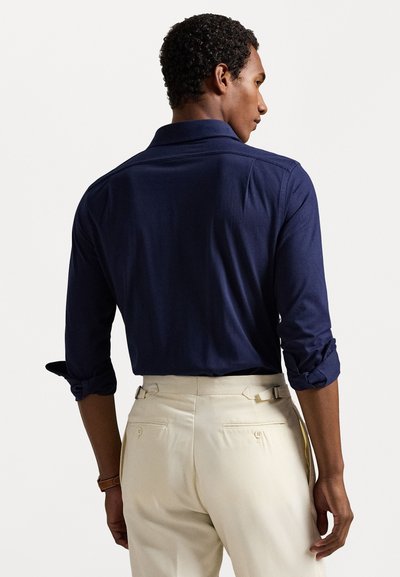 Ναυτικό μπλε μακρυμάνικη μπλούζα με γιακά και διπλωμένα μανίκια, συνδυασμένη με κρεμ παντελόνι που διαθέτει πίσω τσέπες και ρυθμιζόμενα πλάγια κλιπ.