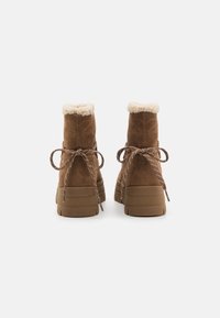 Bottines en suède brun avec doublure en fourrure, semelles épaisses en plateforme et détails texturés. Présente des lacets contrastants noués à l'arrière.