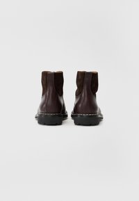 Bottes chelsea en cuir brun avec tige en daim, bout rond, languette de tirage et semelle en caoutchouc épaisse avec des coutures visibles.
