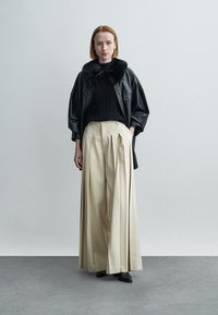 Zwarte leren jas met bontkraag, geribbelde zwarte trui, roomkleurige wijduitlopende geplooide broek, zwarte schoenen, minimalistische achtergrond.