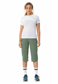 Weißes Kurzarmhemd mit hochgekrempelten Ärmeln, grüne kurze Hose und weiße Socken mit schwarzen Streifen, kombiniert mit blauen Sportschuhen.