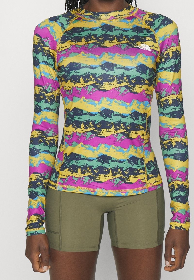 Farverig langærmet rash guard med et bølgemønster i gul, pink, grøn og blå. Lavet af strækbart materiale med en tætsiddende pasform.