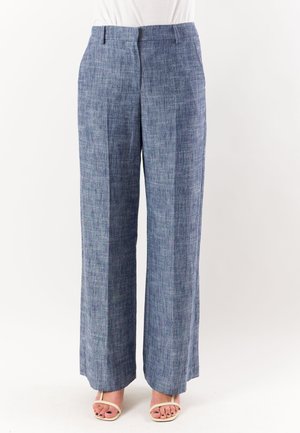 Pantaloni larghi in lino blu con una texture sottile, pieghe frontali e passanti per cintura, indossati con sandali beige con cinturini.