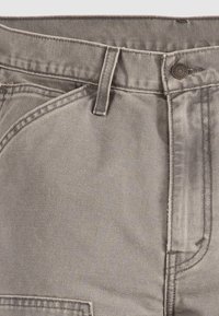 Gros plan sur un pantalon en jean gris montrant les passants de ceinture, une poche avant et une fermeture par bouton métallique.