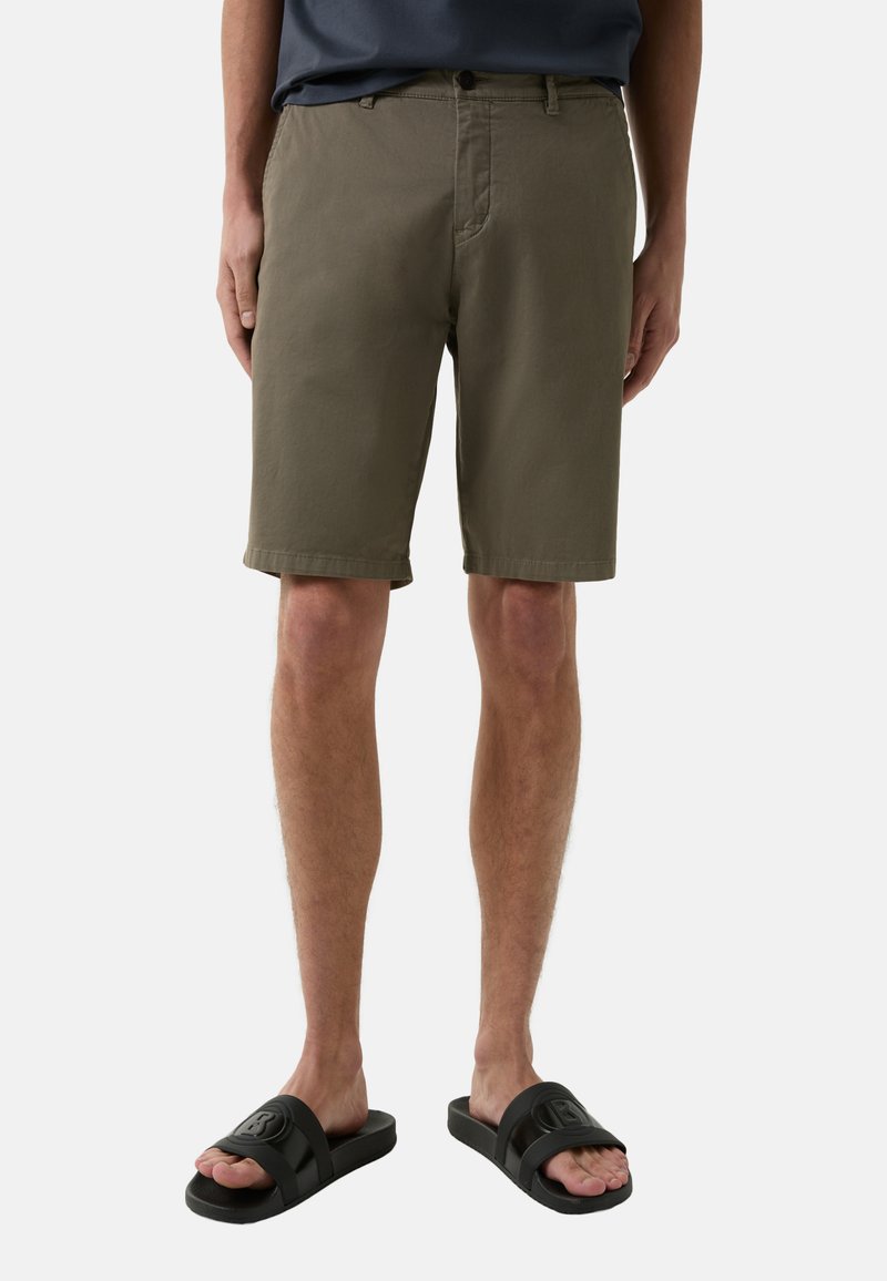 Olivgrüne Baumwollshorts mit lockerer Passform, vorderen Taschen und Knopfverschluss, kombiniert mit schwarzen Gummisandalen mit Logo.