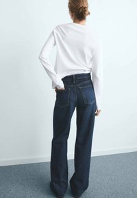 Donkerblauwe high-waisted jeans met een relaxed fit, voorzien van achterzakken en een textuurstof van denim, gecombineerd met een wit longsleeve shirt.