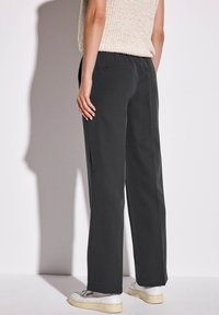 Pantaloni neri a gamba larga realizzati in un tessuto morbido con una texture liscia. Comprendono tasche laterali e si fermano sopra la caviglia, abbinati a sneakers bianche.