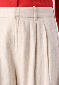 Pantalons en lin beige avec des plis à l'avant, dotés d'une taille plate et d'un tissu texturé pour une finition légère.