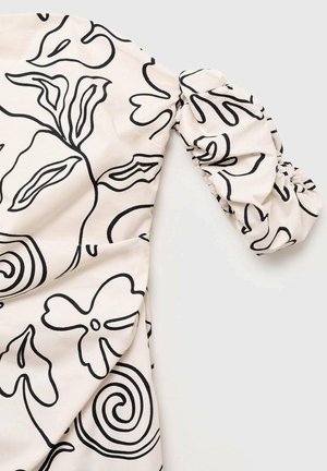 Top in tessuto leggero con sfondo crema e disegni floreali neri in linea. Le maniche a sbuffo presentano dettagli arricciati per aggiungere texture.