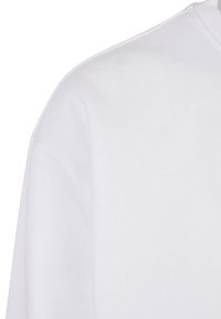Chemise blanche à manches longues et col rond montrant la zone de l'épaule et le haut de la manche sans motifs ni logos visibles.