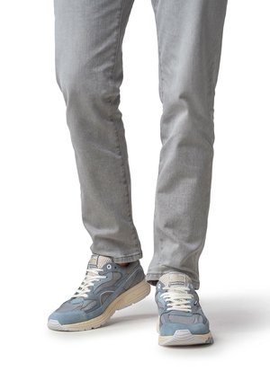 Baskets grises avec une tige en mesh et en daim, présentant un design texturé, des lacets blancs et une semelle en caoutchouc couleur crème. Portées avec un pantalon gris clair.