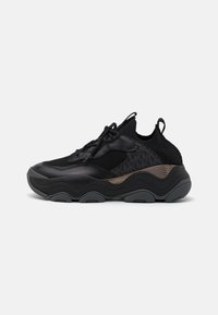 Black athletic shoes with a textured mesh upper, sleek design, and pronounced outsole curve. Features laces and metallic accents.