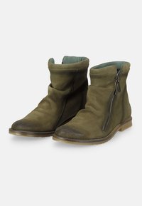 Botas de ante verdes hasta el tobillo con un eje plegado y un cierre lateral. Punta redondeada y una puntera oscura en contraste. Suela de goma plana.