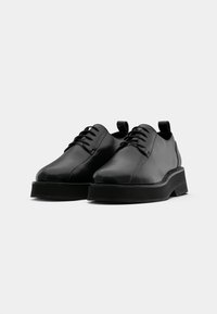 Scarpe in pelle nera con punta arrotondata, design con lacci e suola piatta nera spessa. Tessuto liscio con uno stile minimalista.