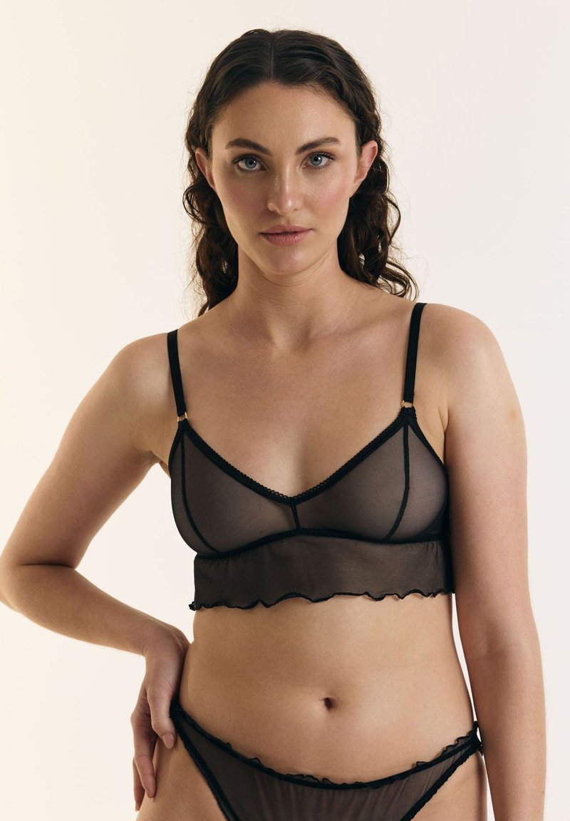 Zwarte doorschijnende bralette met een gegolfde rand, dunne bandjes en gouden accenten. Gecombineerd met bijpassende zwarte doorschijnende bikini slipjes.