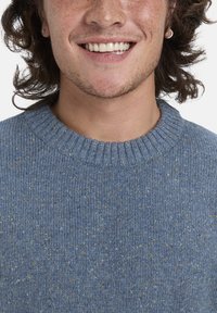 Blauer gestrickter Pullover mit einem strukturierten Muster, ausgestattet mit einem gerippten Halsausschnitt und subtilen Sprenkeln von Gelb und Grün im gesamten Stoff.