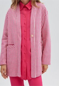 Roze-wit geruit blazer met een ontspannen pasvorm, twee steekzakken aan de voorkant en een enkele knoopsluiting over een felroze shirt.