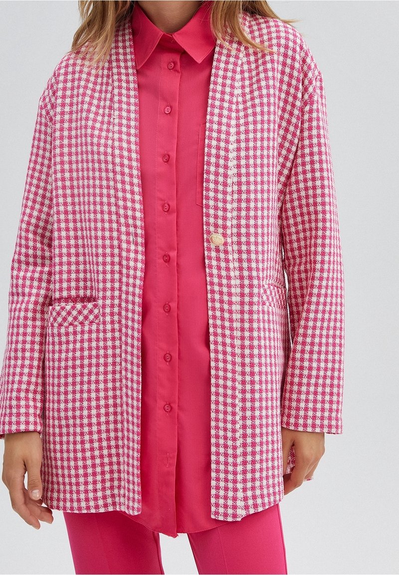 Roze-wit geruit blazer met een ontspannen pasvorm, twee steekzakken aan de voorkant en een enkele knoopsluiting over een felroze shirt.