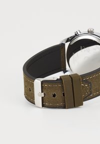 Bracelet de montre en textile marron avec boucle et accents en acier inoxydable argenté, présentant un intérieur noir lisse et un contraste de couture blanche.