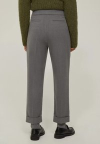 Pantaloni grigi su misura con tasche piatte e due tasche posteriori, dotati di orli a coste e una texture liscia. Indossati con scarpe nere e calzini grigi.