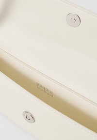 Πορτοφόλι σε κρεμ απόχρωση με λεία δερμάτινη υφή, διαθέτοντας ασημένιο κούμπωμα και εγχαραγμένο λογότυπο στο εσωτερικό. Μινιμαλιστικός σχεδιασμός.