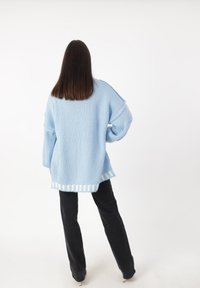 Lichtblauwe oversized trui met geribde manchetten en een gestreepte zoom, gecombineerd met zwarte broek. Zachte, gestructureerde breiwijze.