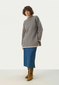 Sweter dzianinowy w wzór jodełki w kolorze beżowym i ciemnoniebieskim, z wysokim kołnierzem, długimi rękawami, noszony na dżinsowej spódnicy i brązowych zamszowych botkach.