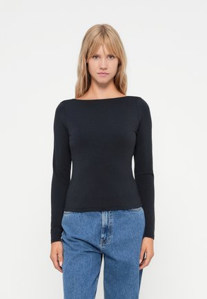 Top negru cu mânecă lungă și decolteu tip barcă, confecționat dintr-un material neted. Asortat cu blugi lejeri de culoare bleu deschis.