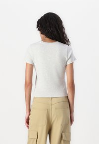 Tricou cu mânecă scurtă, gri deschis, cu decolteu rotund, pereche cu pantaloni cargo bej, cu buzunare laterale și o croială lejeră.