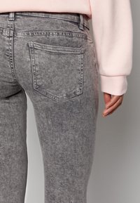 Jeans in denim grigio con una texture sbiadita, taglio stretto e una singola tasca posteriore. La vita presenta passanti per la cintura e dettagli di cucitura.