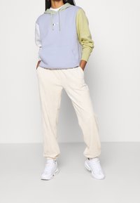 Hoodie i pastellblått, grönt och vitt; har en framficka och en logotyp. Parat med krämfärgade corduroy-joggers och vita sneakers.