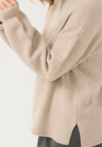 Beiger Wollpullover mit lockerer Passform, gerippten Bündchen, seitlichen Schlitzen und einer weichen, strukturierten Oberfläche.