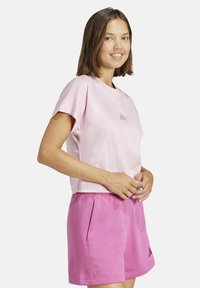 T-shirt di cotone rosa con maniche corte e colletto rotondo, abbinata a pantaloni corti rosa coordinati con tasche laterali e logo Adidas.