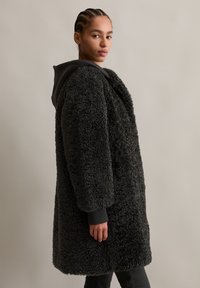 Fluffy donkergrijze jas met een gestructureerd oppervlak, oversized pasvorm en een zwarte capuchon. Lange mouwen met ribbels aan de zomen.