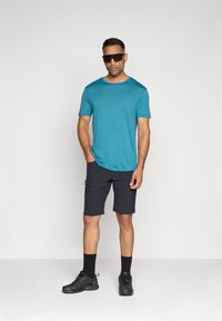 Tyrkis kortermet t-skjorte sammen med svarte shorts. Brukt med mørke solbriller og svarte joggesko med teksturert stoff.