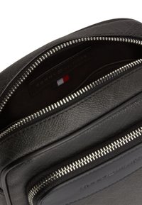 Μαύρη τσάντα Tommy Hilfiger από δέρμα με υφή, με ανοιχτό κεντρικό φερμουάρ και εμφανές λογότυπο μέσα και στην πλαϊνή τάπα του φερμουάρ της μπροστινής τσέπης.